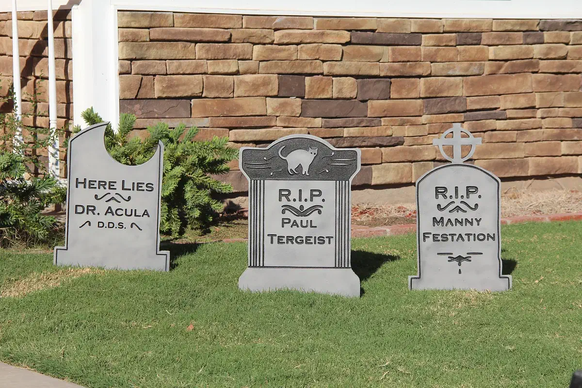 Three finished gray Halloween tombstones with carved names and designs displayed on a lawn