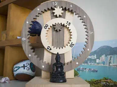 Hanging wooden gear clock with exposed toothed wheels, displayed on a shelf against a coastal backdrop