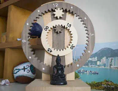 Hanging wooden gear clock with exposed toothed wheels, displayed on a shelf against a coastal backdrop