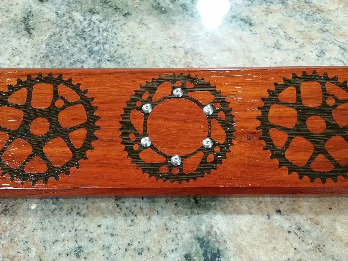 Finished reddish wooden key holder with three dark bicycle gears and six small metal magnets in the center gear