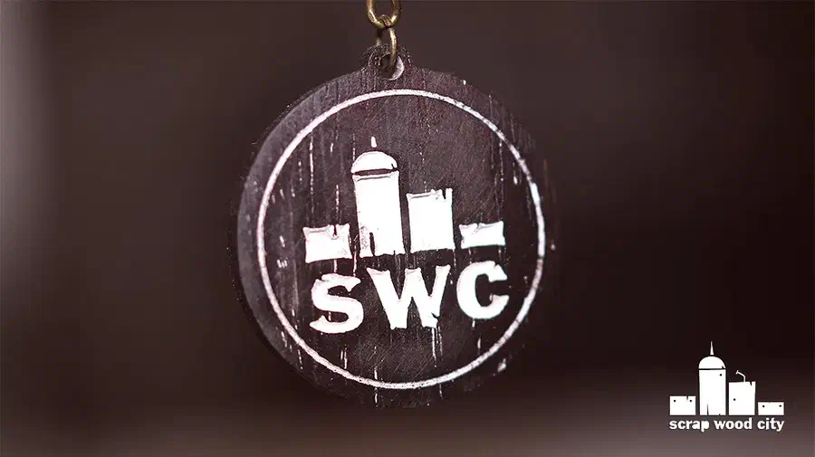 Round dark wooden SWC logo keychain with its complete fob and top attachment hole visible against a blurred brown background
