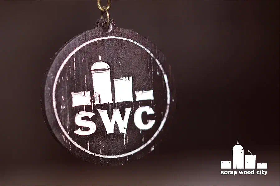 Round dark wooden SWC logo keychain with its complete fob and top attachment hole visible against a blurred brown background