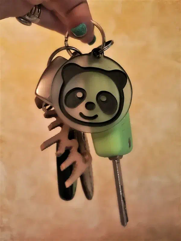 Finished black-and-pale panda keychain hanging from a split ring beside a set of keys, held against a softly blurred tan background