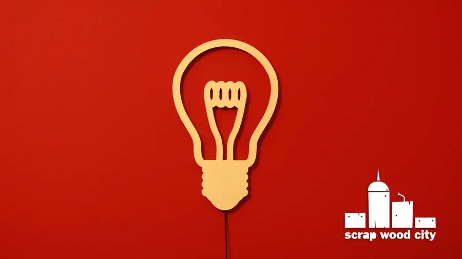 A pale plywood light-bulb outline hanging on a red wall with a black cord