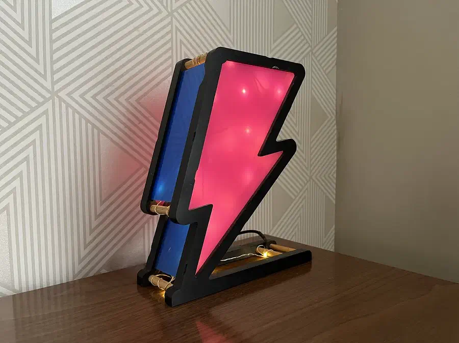 A black-edged lightning-bolt lamp with glowing pink and blue panels on a wooden table