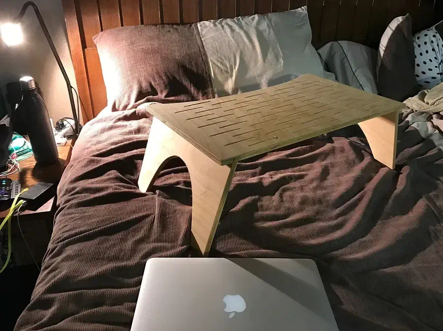 A wooden lap desk with rows of narrow slots standing on curved legs on a bed