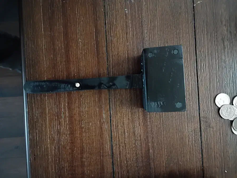A dark laminated plywood mallet lying sideways on a wooden surface, with dowel ends visible