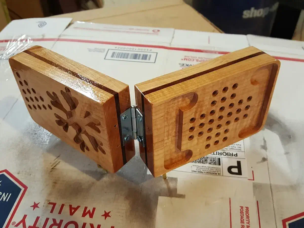Hinged maple game case with drilled game holes and a carved starburst, photographed on shipping packaging