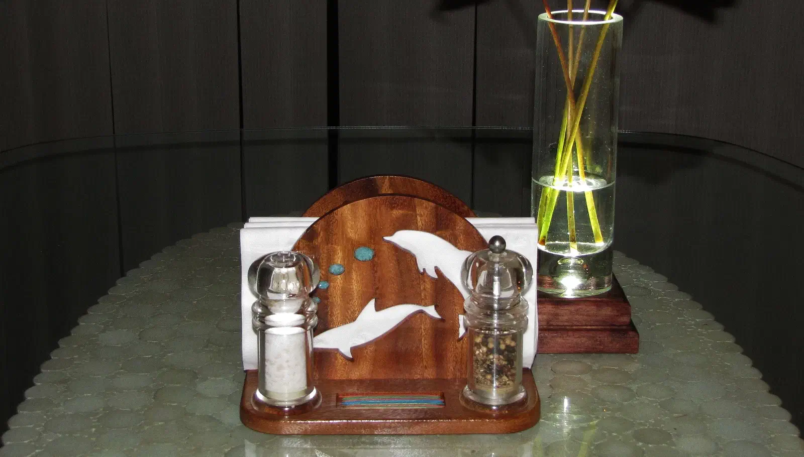 Finished wooden dolphin napkin stand with turquoise-colored accents, paper napkins, salt and pepper shakers and a rectangular pocket in the base