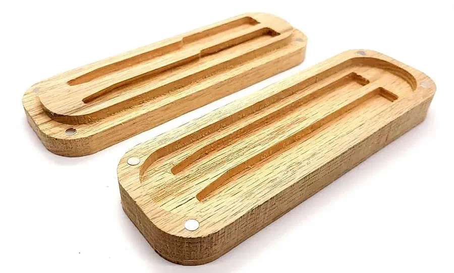 Two open oak case halves with long pen recesses and small round closure pockets on a white background