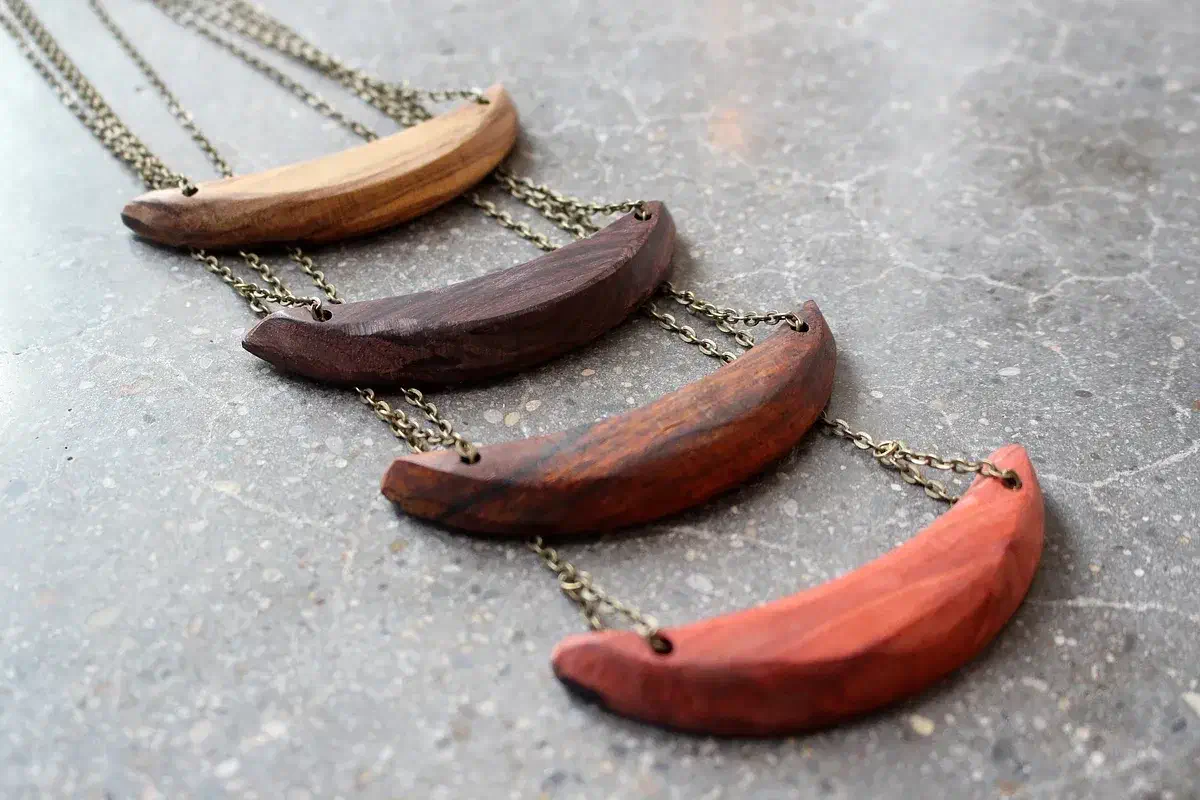 Four curved wooden necklace pendants in pale, dark and reddish wood with metal chains