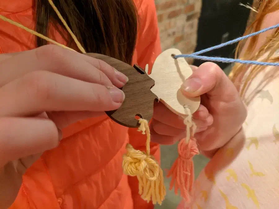 Two hands holding matching pale and dark wooden butterfly charms with blue cords and yarn tassels