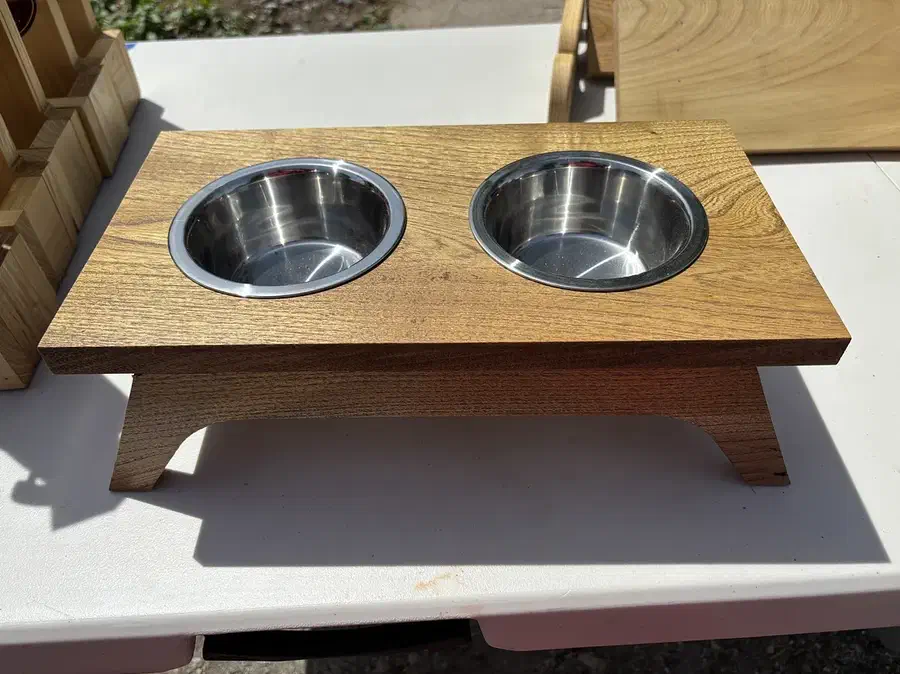 A complete low wooden pet feeder with a rectangular walnut top, two removable metal bowls and shaped supports underneath.