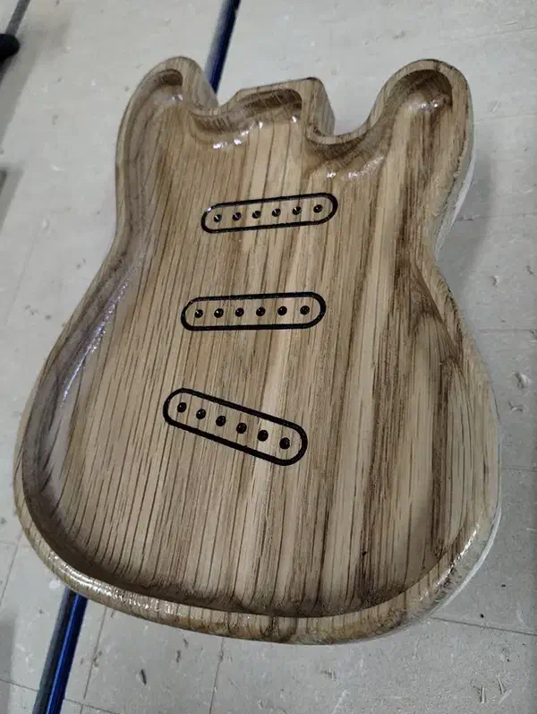 A glossy wooden guitar-body tray with three black pickup-shaped engravings inside its pocket