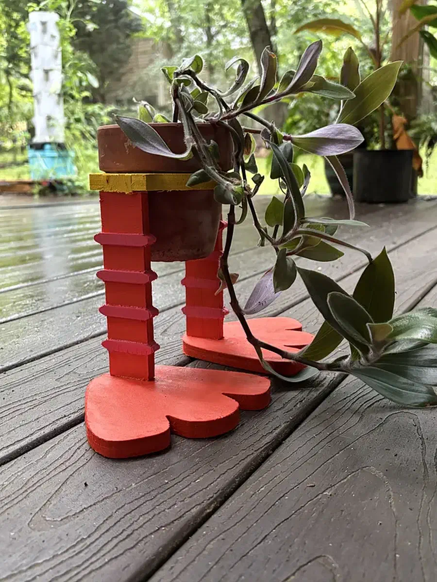 A plant pot on a painted plywood stand with red bird feet and ribbed legs on a deck