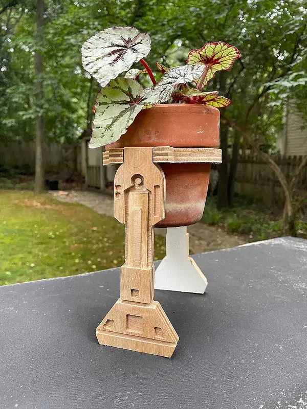 A terracotta plant pot on an unpainted wooden stand with robot-like legs and broad feet