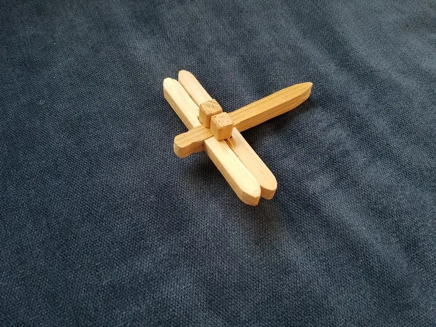 Assembled pale wooden dragonfly puzzle with crossed wings and two small locking pieces on dark fabric