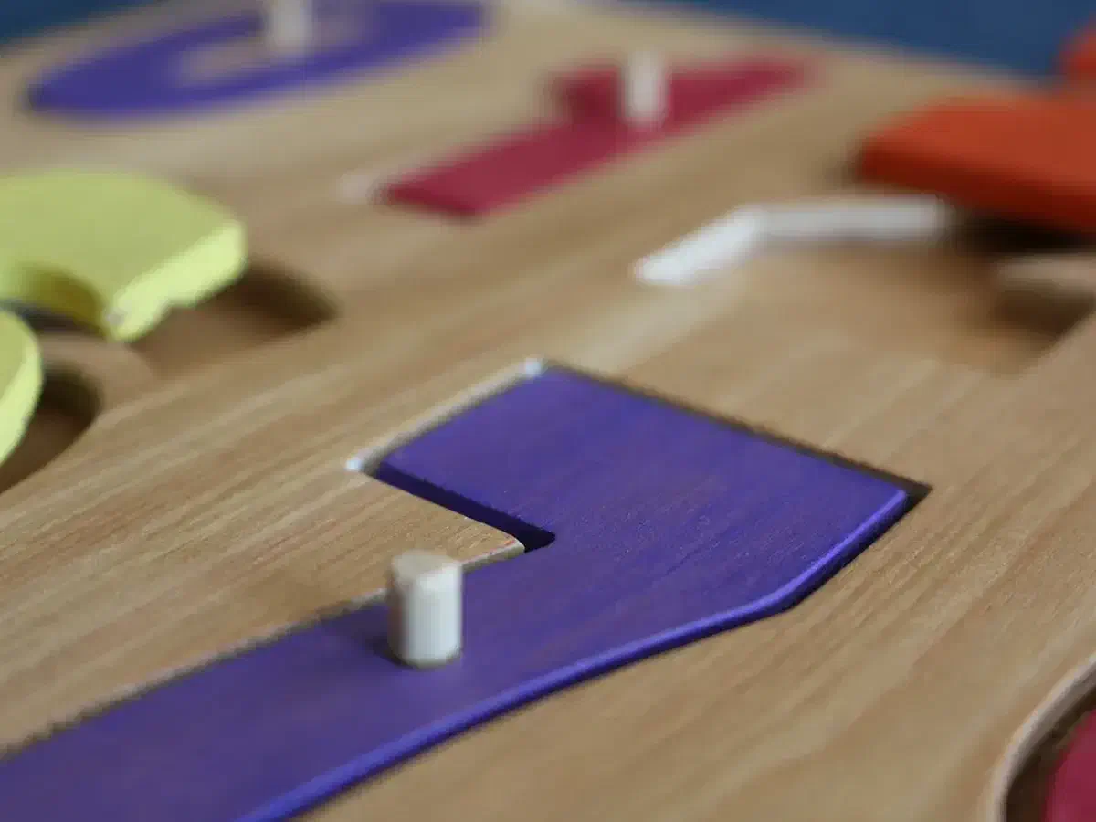 Close view of a purple wooden number seven with a small dowel knob seated in a plywood puzzle board
