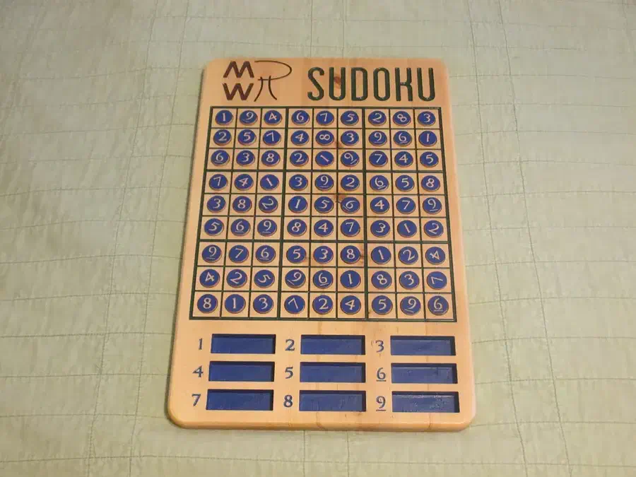Wooden Sudoku board filled with blue numbered pieces, with nine spare-piece pockets below the grid