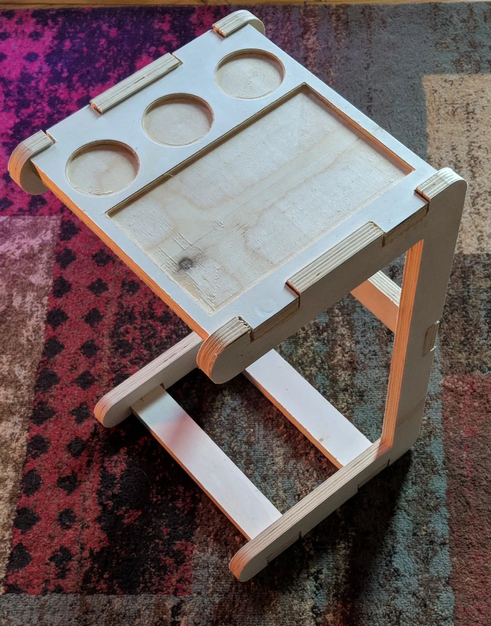 A pale plywood sofa table with an open C-shaped frame, three round cup recesses and a rectangular tray recess