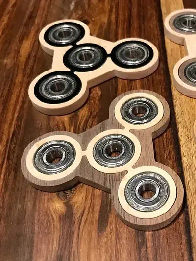 Two complete wooden three-armed spinners with contrasting inlay borders and installed bearings on a wooden surface