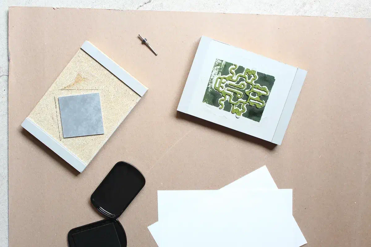A green linoleum block print on a white card beside its carved stamp and ink pad
