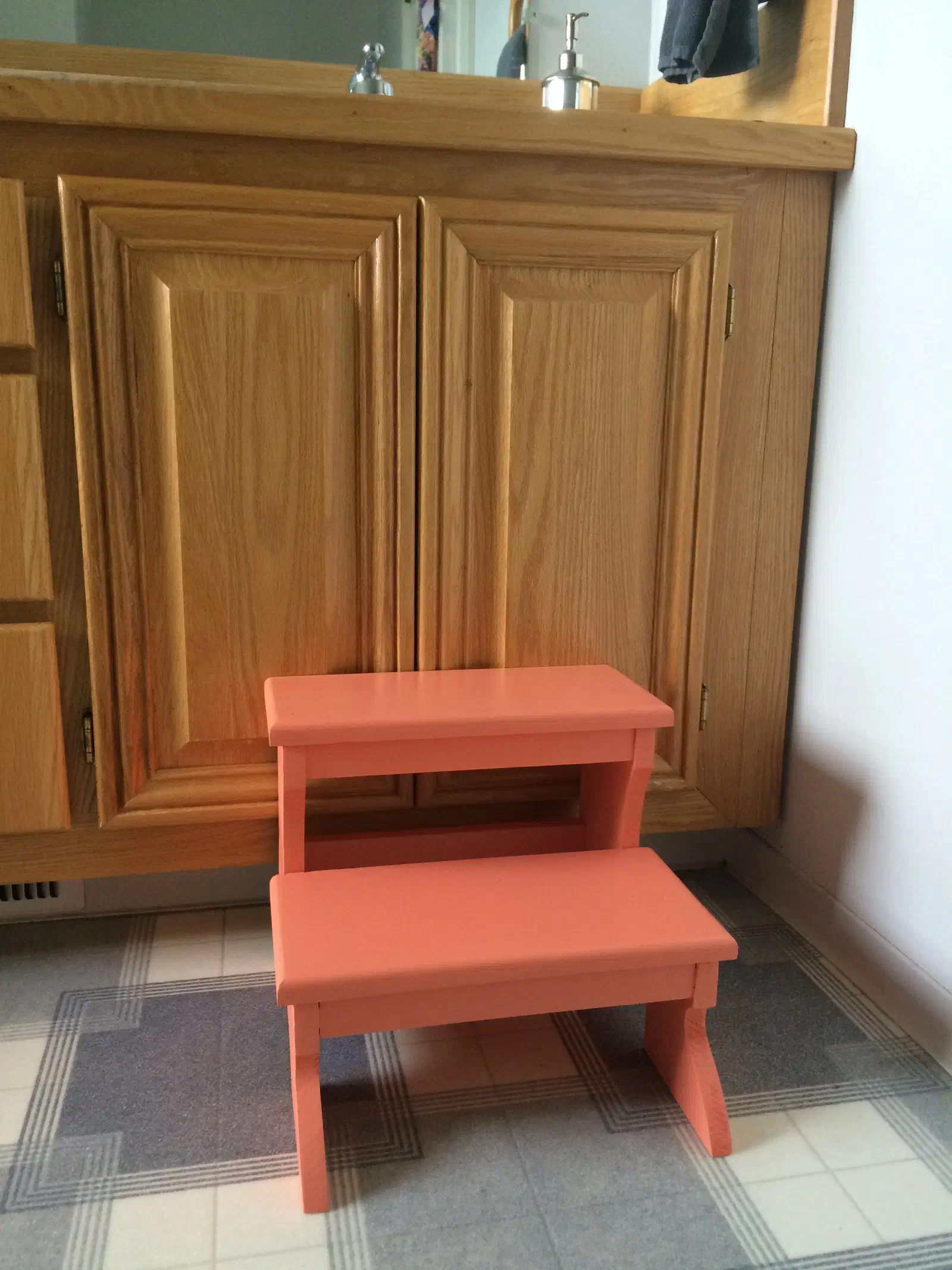 A red painted two-step stool standing in front of a wooden bathroom cabinet