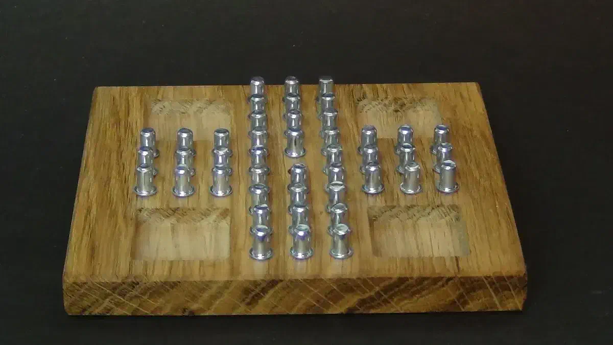 A finished hardwood peg-solitaire board populated with chromed shelf pins