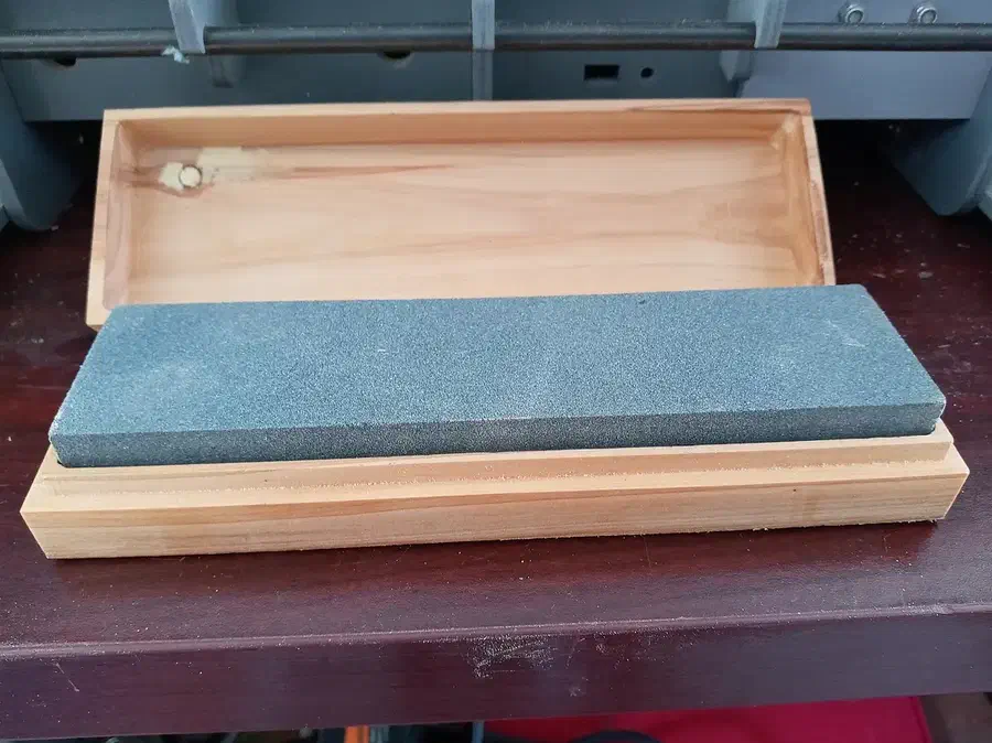 An open pine sharpening-stone box with a gray stone seated above its base