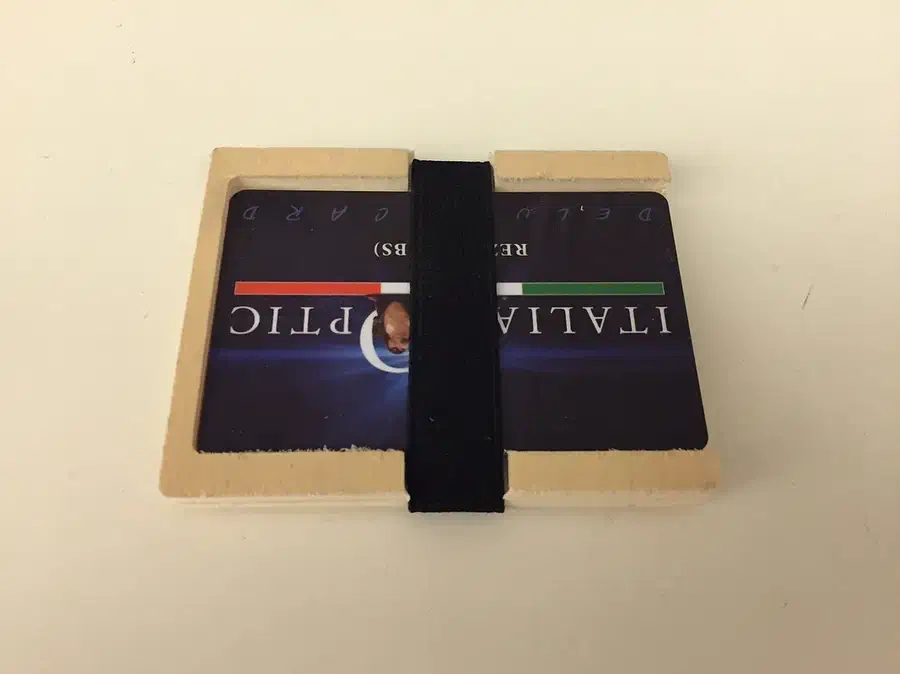 A plywood pocket card holder with cards secured beneath a black elastic band