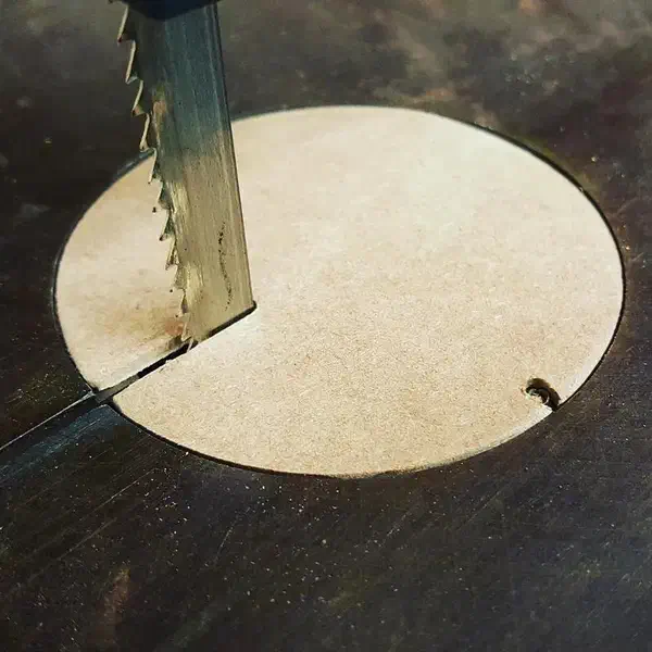 A pale circular bandsaw throat plate with a blade-entry slit and small locating notch