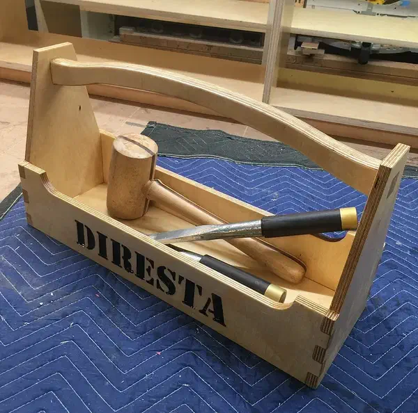 Jimmy DiResta’s finished plywood tote with its complete curved handle, mallet and chisels inside, on a blue quilted blanket.