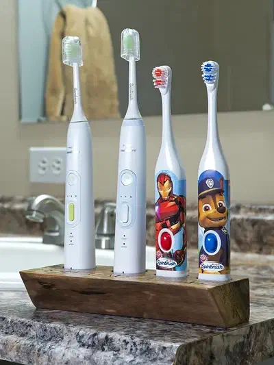 Four complete electric toothbrushes stand in a walnut holder on a bathroom counter, with the entire wooden base visible.
