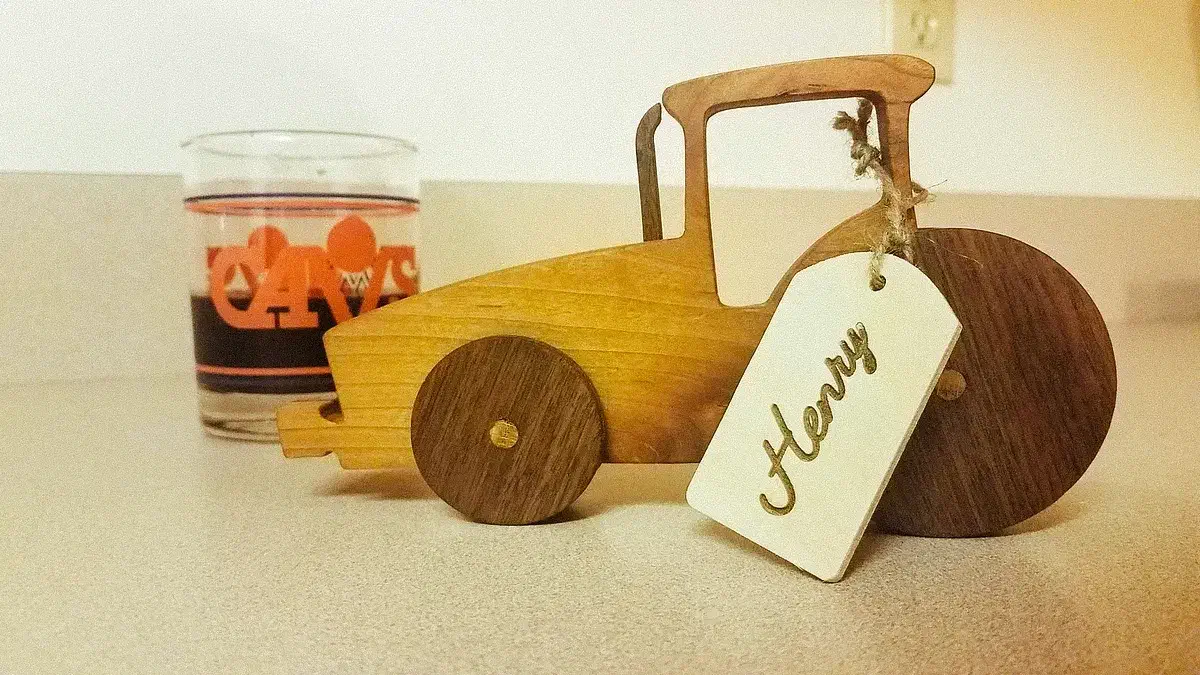 A wooden tractor with a tall cab, large dark rear wheel and a gift tag tied around its body