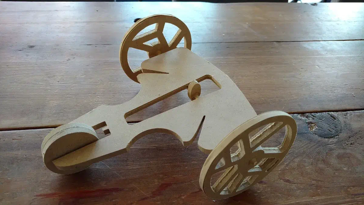 An open wooden rubber-band racer with patterned spoke wheels and a stretched band on a dark table