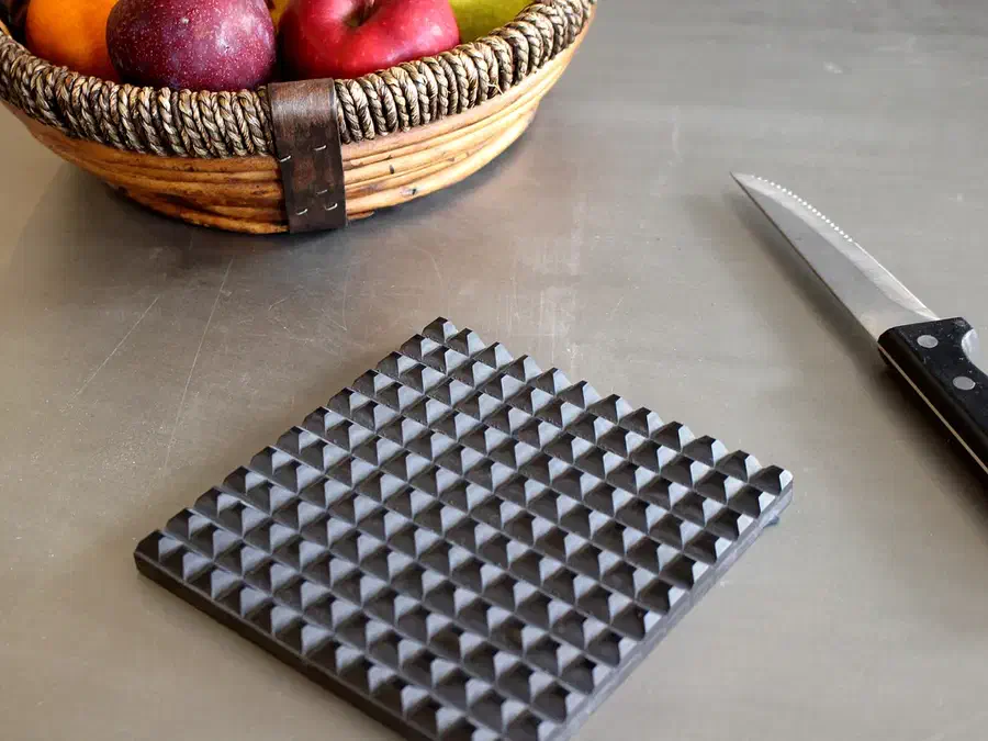 Dark Corian trivet with a raised grid of pointed studs on a kitchen counter