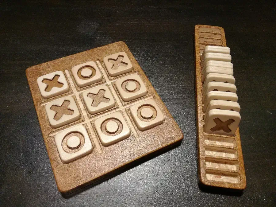 A wooden tic-tac-toe board filled with X and O pieces beside a narrow wooden piece rack
