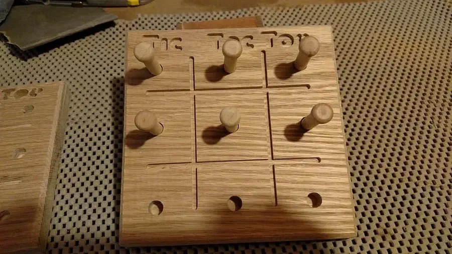 A small hard-maple tic-tac-toe board with wooden pegs standing in several playing holes