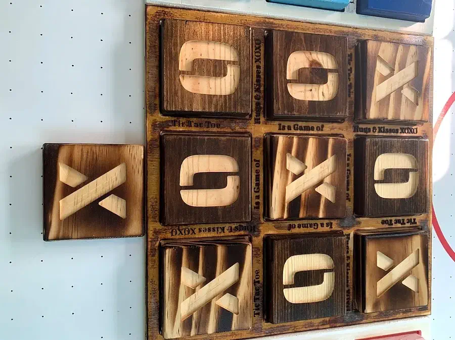 A wooden tic-tac-toe board filled with large square tiles carrying raised X and O shapes