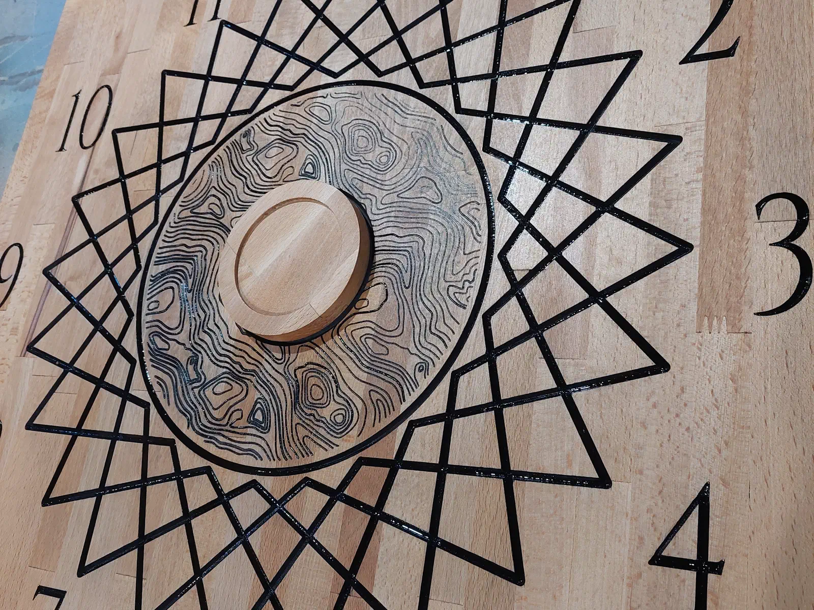 Hard-maple clock face with black numerals and a geometric star pattern around its round center