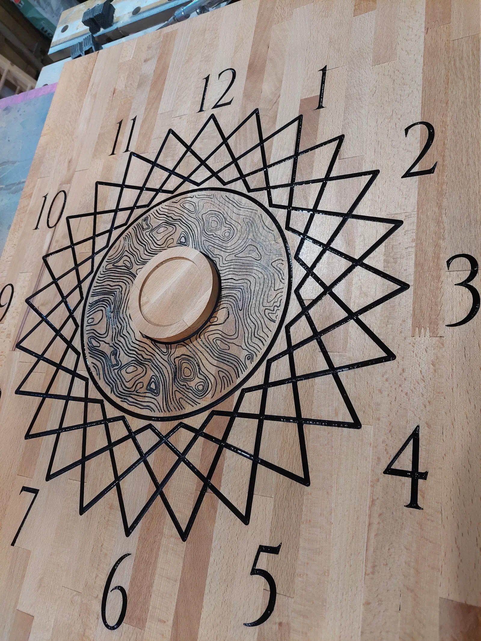 Hard-maple clock face with black numerals and a geometric star pattern around its round center