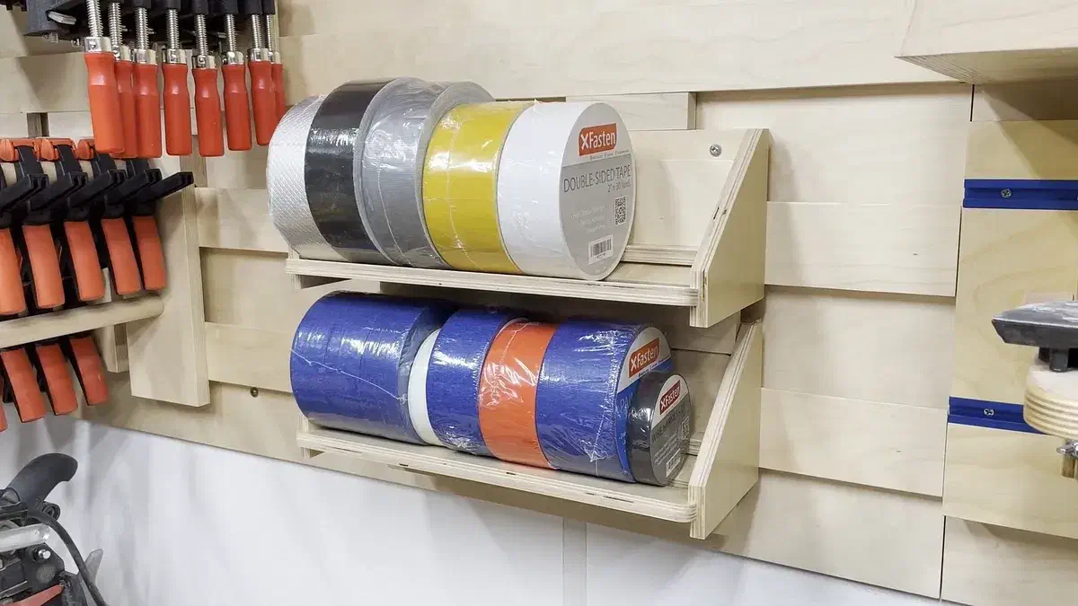 Two wooden wall racks holding rolls of colored tape on sloping shelves