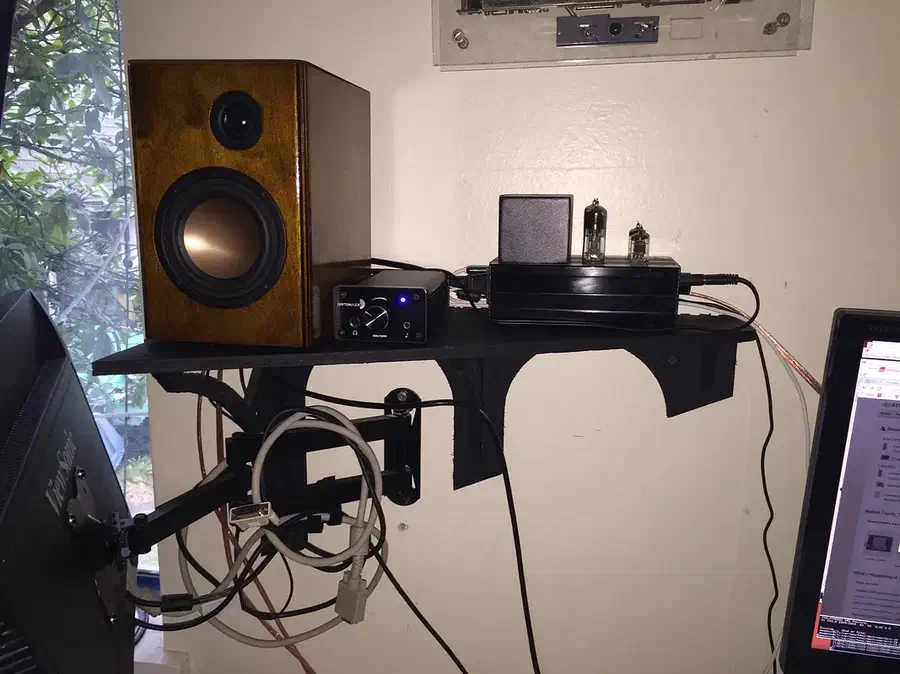 A black wall shelf holding a speaker and electronic equipment above a desk