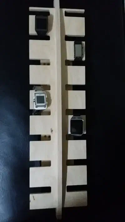 A tall pale plywood wall rack with watches hanging from projecting arms against a dark background