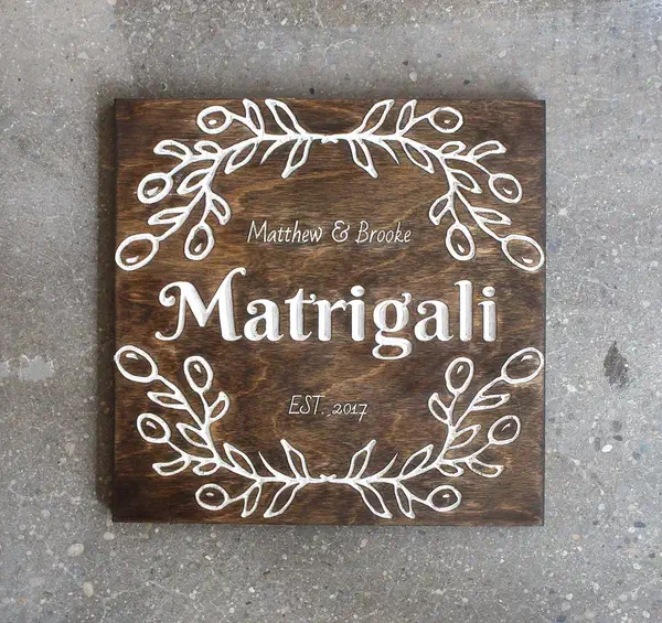 Finished square dark-stained wood wedding sign with white carved names, surname, date, and leafy border