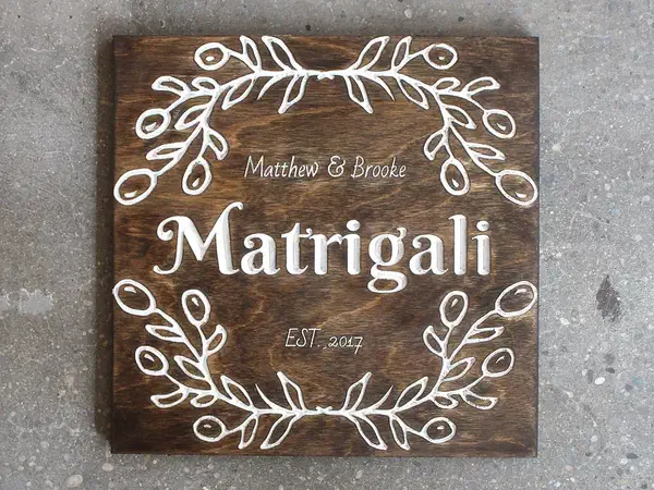 Finished square dark-stained wood wedding sign with white carved names, surname, date, and leafy border