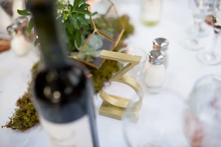 Finished cream-colored standing number three on a wedding table beside greenery and glassware