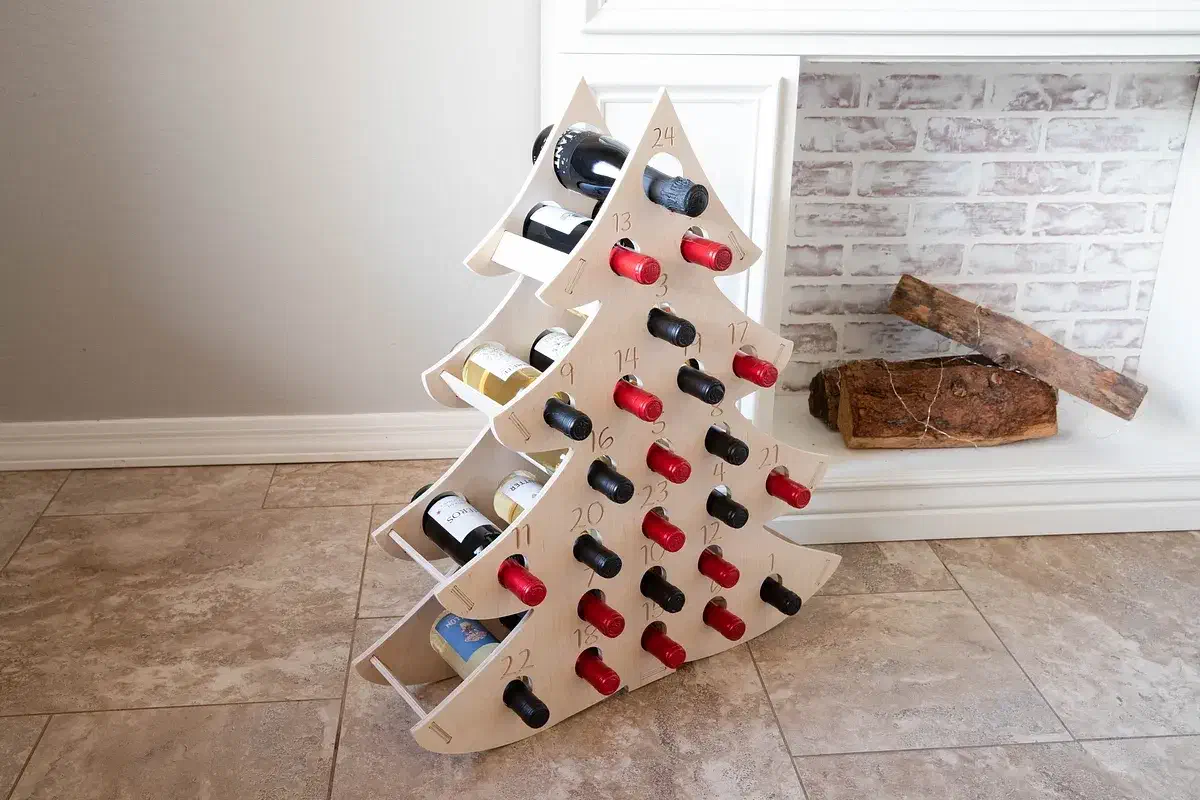 A wooden Christmas-tree bottle rack filled with wine bottles beside a fireplace
