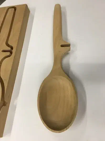 A carved wooden spoon with an oval bowl and long handle beside its remaining wood blank