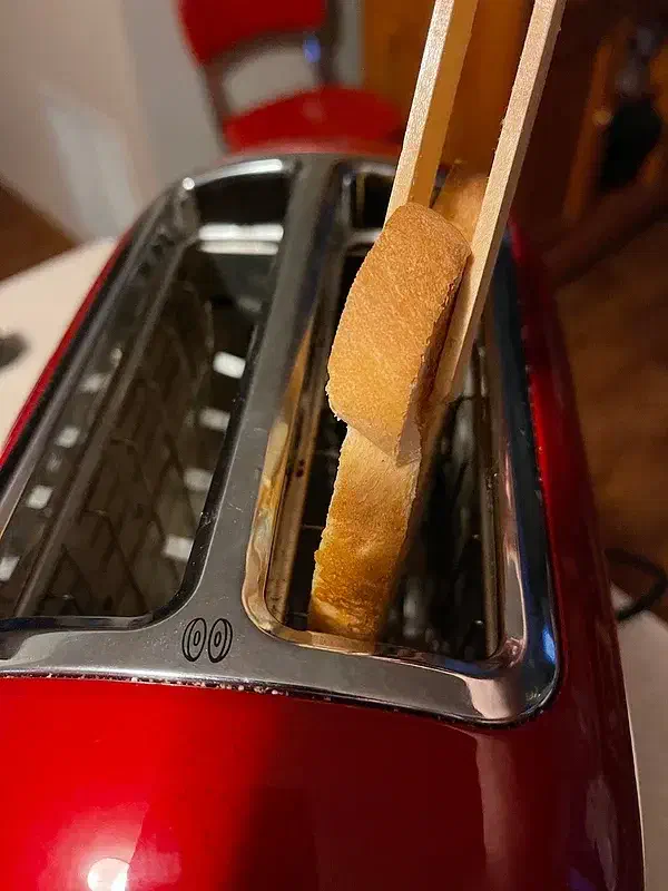 Wooden tongs lifting a slice of toast from a red toaster